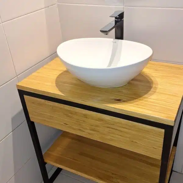 Lavabo moderno con encimera de madera, grifo metálico y espejo redondo en baño con azulejos blancos.