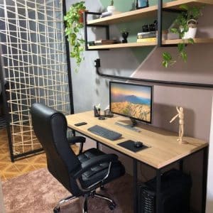 Escritorio moderno con superficie de madera y estructura metálica, equipado para trabajo en casa; incluye silla ergonómica, estantería con plantas y accesorios decorativos. Ideal para productividad.