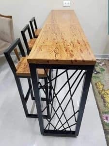 Barra alta de madera con tres sillas de respaldo cuadrado y estructura metálica. Ideal para cocina moderna o reuniones sociales en espacios pequeños. Diseño contemporáneo y funcional.