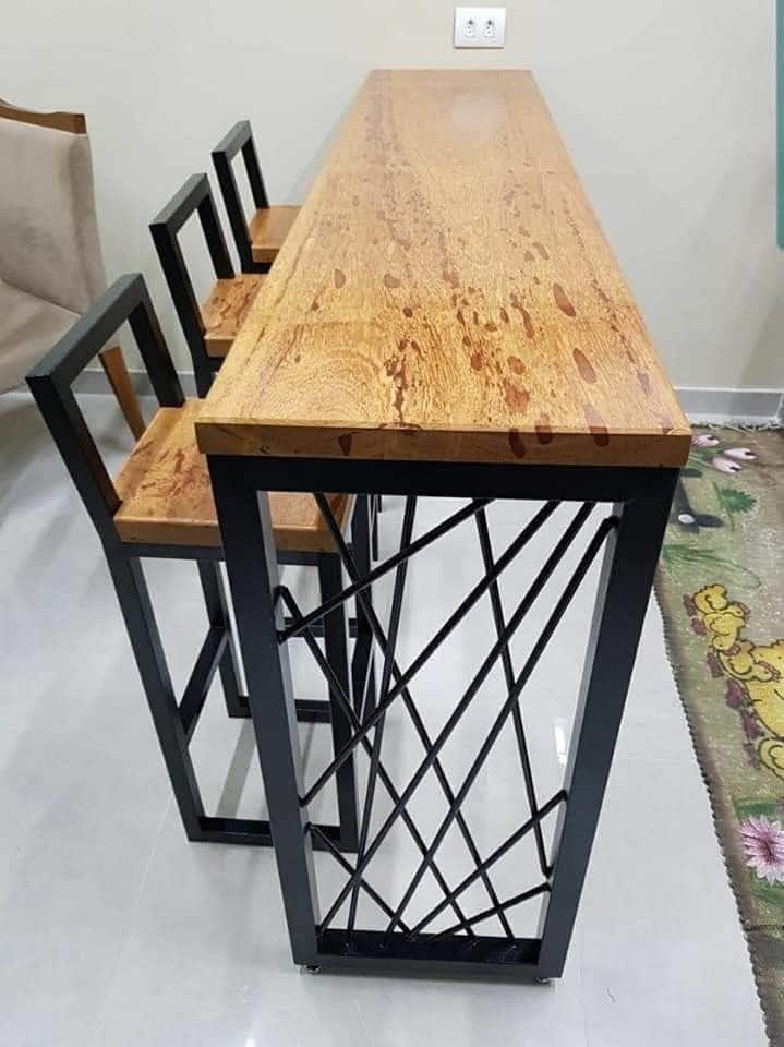 Barra alta de madera con tres sillas de respaldo cuadrado y estructura metálica. Ideal para cocina moderna o reuniones sociales en espacios pequeños. Diseño contemporáneo y funcional.