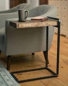 Mesa auxiliar moderna con estructura metálica negra y tablero de madera rústica, ideal para usar junto a un sillón. Diseño funcional y elegante para ambientes contemporáneos.