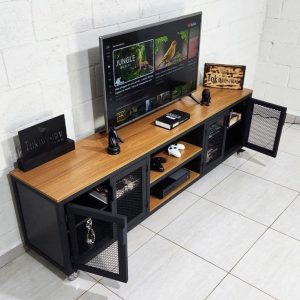 Mueble de TV con superficie de madera y estructura negra, puertas de malla metálica, amplios compartimentos para tecnología y objetos decorativos sobre piso de baldosas blancas.