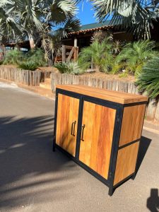 Gabinete de madera con dos puertas, marco metálico negro, mangos oscuros. Diseño moderno y rústico, ideal para exteriores o interiores con estilo industrial.