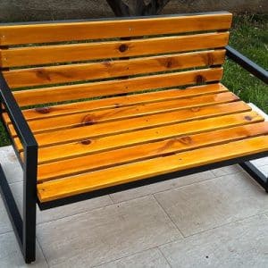 Banco de jardín con tiras de madera barnizada en tonos amarillos sobre una estructura metálica negra. Ideal para exteriores, combina estética moderna y funcionalidad duradera.