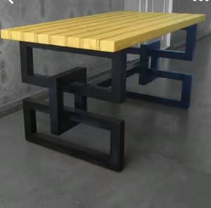 Mesa moderna con tablero de madera clara y patas de metal negro en un diseño geométrico entrelazado. Ideal para ambientes contemporáneos.