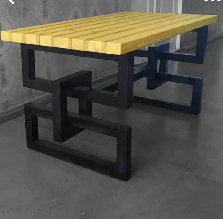 Mesa moderna con tablero de madera clara y patas de metal negro en un diseño geométrico entrelazado. Ideal para ambientes contemporáneos.