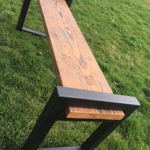 Banco rústico de madera con estructura metálica negra en ambos extremos, ubicado en un jardín con césped verde. Diseño moderno y minimalista para espacios exteriores.