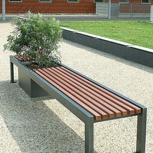 Banco de exterior con estructura de metal negro y listones de madera. Incluye una maceta integrada con arbusto. Diseño moderno y minimalista, ubicado en un área pavimentada.