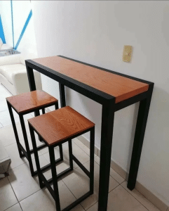 Mesa alta de madera con estructura metálica negra, acompañada de dos taburetes a juego con diseño minimalista, ideal para espacios modernos.