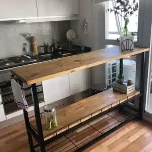 Isla de cocina de madera y metal negro, con dos estantes inferiores para almacenamiento. Diseño moderno, ideal para espacios pequeños y decoración contemporánea.