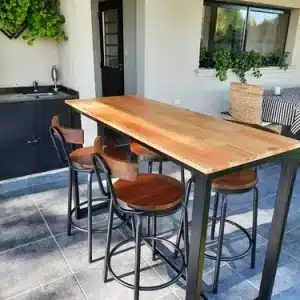 Mesa alta de madera con estructura metálica negra acompañada de cuatro sillas altas con respaldo de madera y patas metálicas, ubicada en un espacio moderno de terraza.