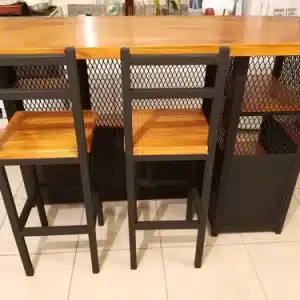 Mesa alta de madera con dos sillas a juego. La estructura es metálica con estantes laterales y un diseño de rejilla negra. Adecuada para cocina o bar.