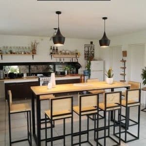 Mesa alta de madera con estructura de metal negro, rodeada de seis banquetas a juego. Diseño minimalista y moderno ideal para cocina o bar.