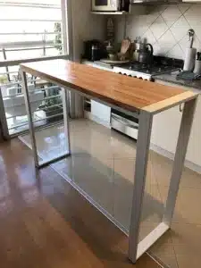 Mesa alta moderna con tablero de madera y estructura metálica geométrica en una cocina, ideal como barra de desayuno o espacio de trabajo funcional y estilizado.