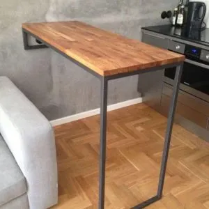 Mesa alta de madera con soporte lateral de metal negro, diseño minimalista flotante, sobre un suelo de parquet claro.