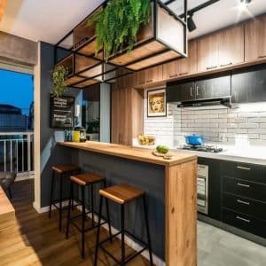 Barra de cocina moderna de madera con tres taburetes altos. Diseño minimalista con estantería suspendida de metal negro y decoración de plantas colgantes.