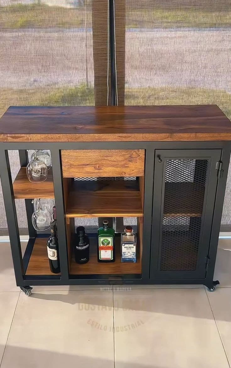 Mueble de bar estilo industrial con estructura de metal negro, repisas de madera, compartimiento de rejilla y ruedas, ideal para almacenar botellas y utensilios de bar.