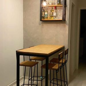 Mesa alta de madera con estructura de metal negro, acompañada de cuatro taburetes a juego. Estante superior con luces LED y botellas de licor exhibidas elegantemente.