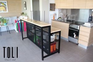 Isla de cocina moderna con estructura de metal negro y superficie de madera clara. Incluye almacenamiento con rejillas para utensilios de cocina. Estilo contemporáneo y funcional.