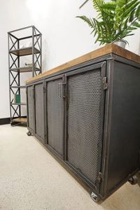 Gabinete industrial de metal con cuatro puertas de rejilla y superficie de madera. Está montado sobre ruedas para facilitar su movilidad. Ideal para espacios modernos y funcionales.