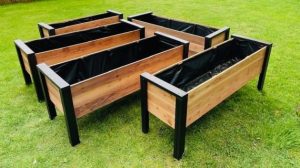 Conjunto de jardineras rectangulares de madera con estructura de metal negro, ideales para huertos urbanos. Diseñadas para exteriores, se destacan sobre el césped verde.