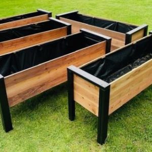 Conjunto de jardineras rectangulares de madera con estructura de metal negro, ideales para huertos urbanos. Diseñadas para exteriores, se destacan sobre el césped verde.