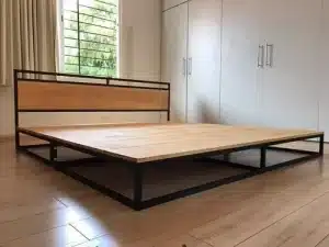 Cama de plataforma moderna con estructura de metal negro y base de madera clara. Respaldo simple. Diseño minimalista en habitación con piso de madera clara y armario blanco integrado.