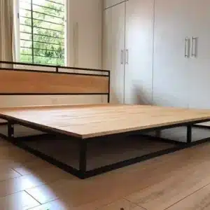 Cama de plataforma moderna con estructura de metal negro y base de madera clara. Respaldo simple. Diseño minimalista en habitación con piso de madera clara y armario blanco integrado.