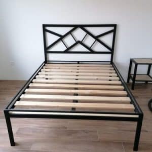 Estructura de cama de metal negro con cabecera geométrica y listones de madera, situada en una habitación con suelo laminado.