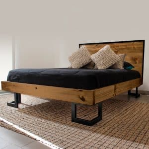 Cama moderna de madera natural con cabecera rústica. Base robusta de metal negro y colchón oscuro, complementada con cojines texturizados. Ideal para un dormitorio contemporáneo.