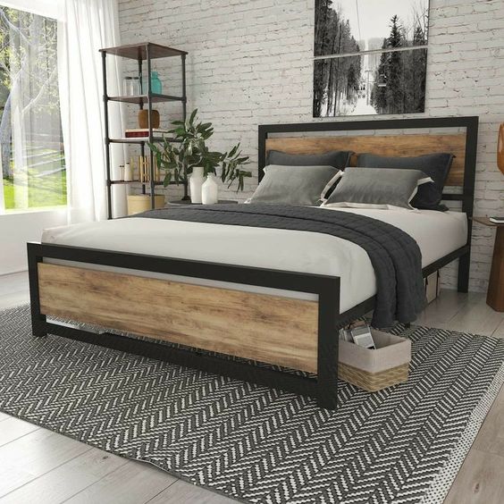 Cama de madera y metal en habitación moderna, con cabecero y piecero de acabado rústico, sobre alfombra de diseño en zigzag.