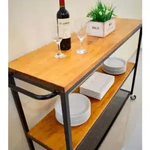 Carrito de cocina con estructura metálica negra y tres estantes de madera. Incluye platos, copas y una caja decorativa sobre la superficie superior.
