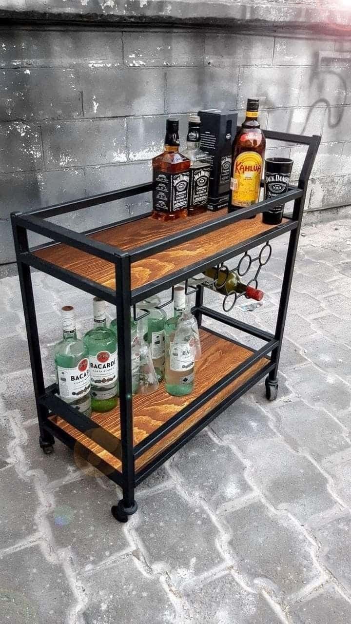 Carrito de bar de metal negro con estantes de madera, ruedas y soporte para botellas. Diseño industrial y funcionalidad ideal para almacenar y servir bebidas.