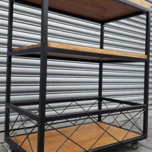 Carrito de almacenamiento industrial de tres niveles, estructura metálica negra con estantes de madera y ruedas grises en la base para facilitar el movimiento.