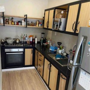 Cocina con muebles de estilo moderno en madera clara y estructura de hierro negro. Incluye armarios con puertas y estanterías abiertas, combinando funcionalidad y diseño elegante.