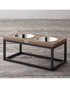 Mueble moderno para mascotas con marco negro de metal y superficie de madera, sostiene dos cuencos de acero inoxidable para comida y agua. Diseño elegante y funcional.