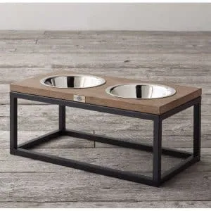 Mueble moderno para mascotas con marco negro de metal y superficie de madera, sostiene dos cuencos de acero inoxidable para comida y agua. Diseño elegante y funcional.