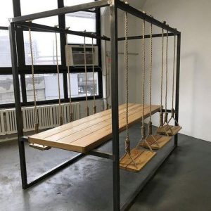 Mesa de comedor moderna con estructura metálica y sillas colgantes tipo columpio de madera, ideales para un ambiente urbano y original.