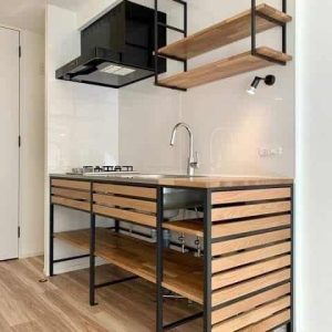 Cocina moderna minimalista con mueble de madera y metal negro, estantes abiertos, fregadero, placas de gas y campana extractora. Ideal para espacios pequeños y diseño contemporáneo.