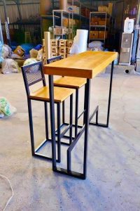 Mesa alta y dos taburetes de madera con estructura metálica negra. Diseño moderno e industrial ideal para espacios pequeños o minimalistas.