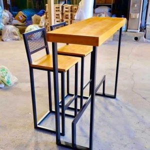 Mesa alta y dos taburetes de madera con estructura metálica negra. Diseño moderno e industrial ideal para espacios pequeños o minimalistas.