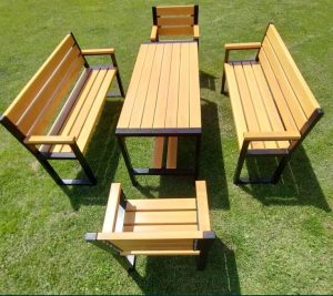 Juego de muebles de jardín con estructura de metal negro y listones de madera clara: una mesa rectangular, dos bancos con respaldo y dos sillas, ubicados sobre césped verde.