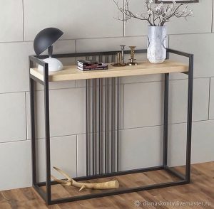 Mesa consola moderna con estructura metálica negra y superficie de madera clara, decorada con libros, lámpara y accesorios. Diseño minimalista ideal para entradas o salas.