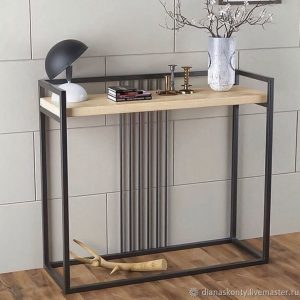 Mesa consola moderna con estructura metálica negra y superficie de madera clara, decorada con libros, lámpara y accesorios. Diseño minimalista ideal para entradas o salas.