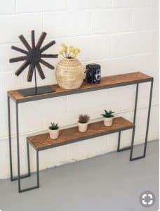 Mesa consola moderna con estructura metálica negra y estantes de madera en espiga. Incluye dos niveles para exhibición de objetos decorativos. Ideal para interiores minimalistas.