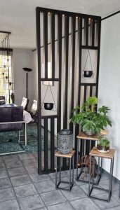 Panel decorativo de madera y metal negro, con diseño geométrico y macetas colgantes. Acompañado de mesas auxiliares con plantas y lámparas. Ideal para separar ambientes modernos.