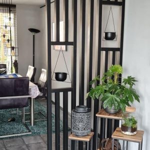 Panel decorativo de madera y metal negro, con diseño geométrico y macetas colgantes. Acompañado de mesas auxiliares con plantas y lámparas. Ideal para separar ambientes modernos.