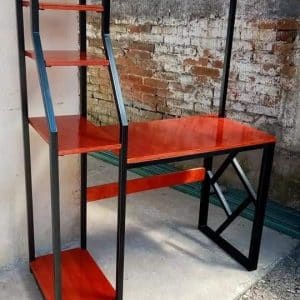 Escritorio con estantes de madera roja y estructura de metal negro. Diseño moderno y funcional, ideal para espacios de trabajo o estudio en interiores de aspecto industrial.