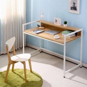 Escritorio minimalista con tablero de madera y estructura metálica blanca, incluye repisa integrada. Ideal para oficina en casa, acompañado de silla de madera y detalles decorativos.