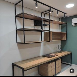 Mueble de oficina moderno con estantes de madera y estructura metálica negra, incluye escritorio largo con cajonera y unidad de repisas superiores con diseño geométrico minimalista.
